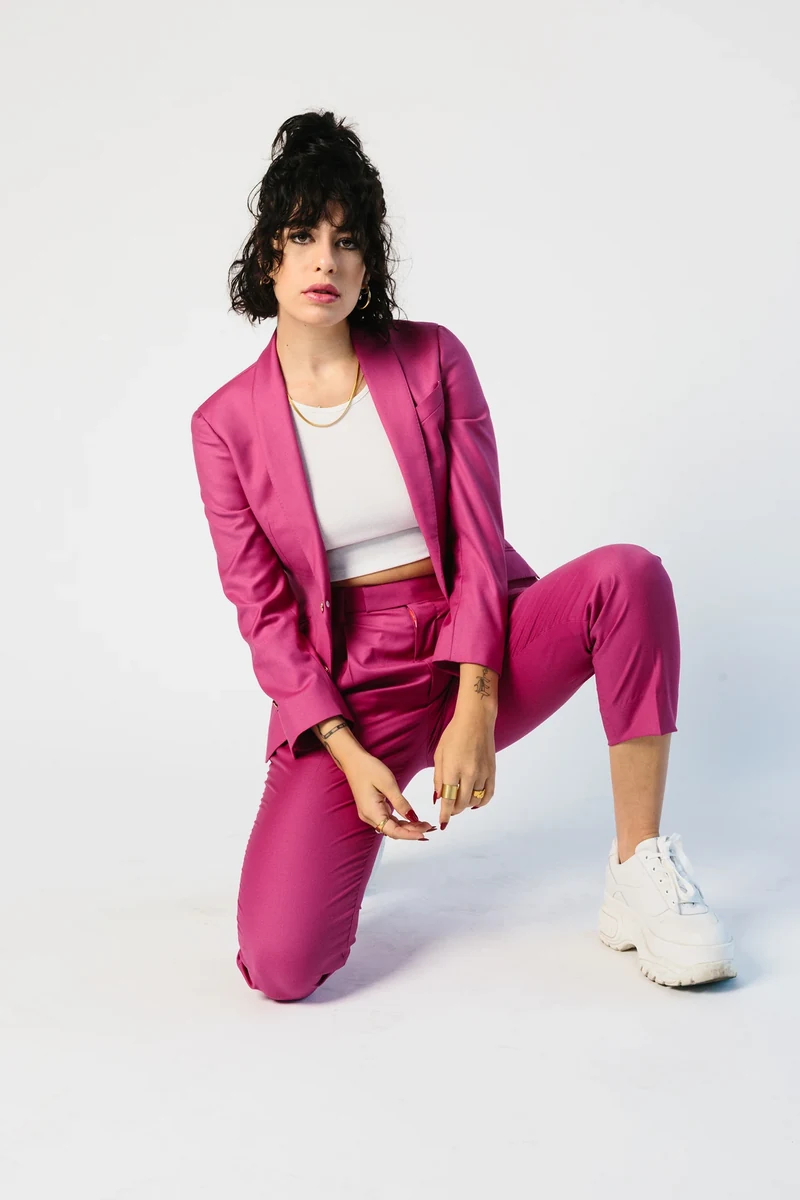 Full portrait of a model in a magenta suit, white crop top, and sneakers.