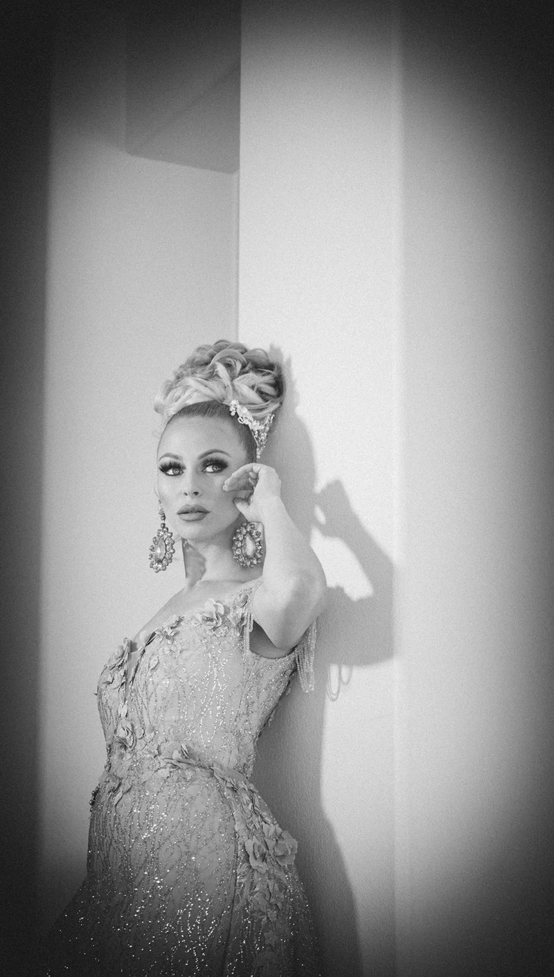 Monochrome full-length beauty portrait beside a bright wall.