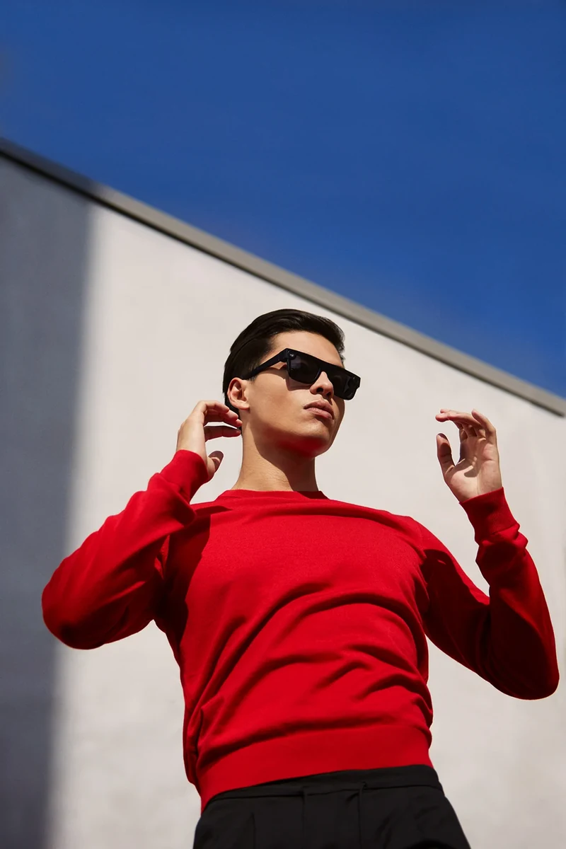 Model wearing black Spectacles and a red sweater beneath a blue sky.